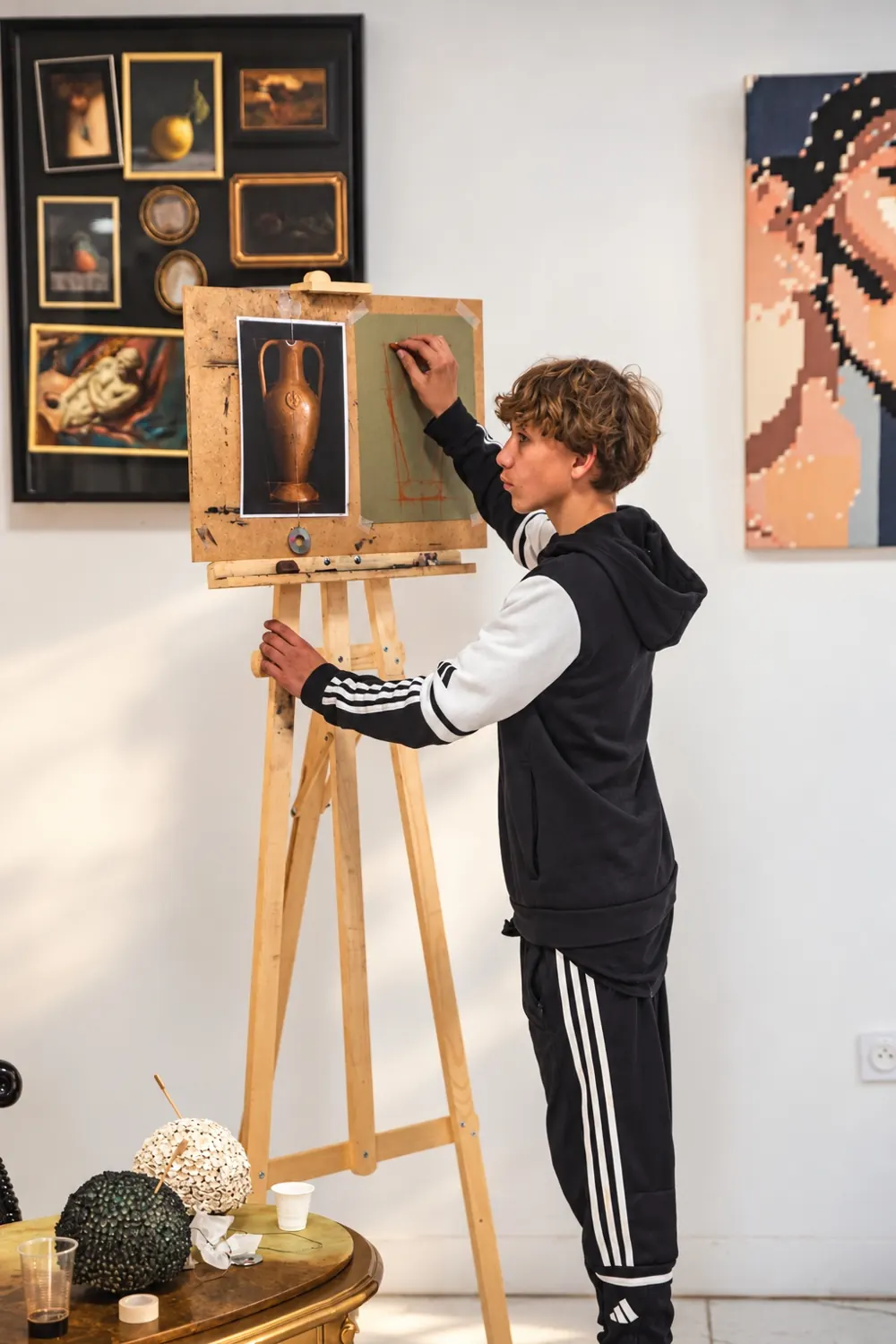 Un adolescent dessine à la sanguine au chevalet dans la galerie